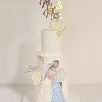 A two-tier wedding cake with a gold Mr & Mrs topper and a painted couple